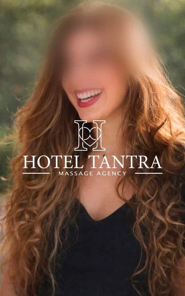 Smiling woman with long wavy hair outdoors; promo overlay reads 'Hotel Tantra Massage Agency' with a decorative logo in the center.