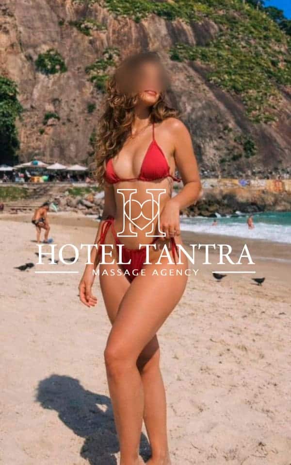Promotional image of a woman in a red bikini standing on a sunny beach, with a 'Hotel Tantra Massage Agency' watermark across her torso.