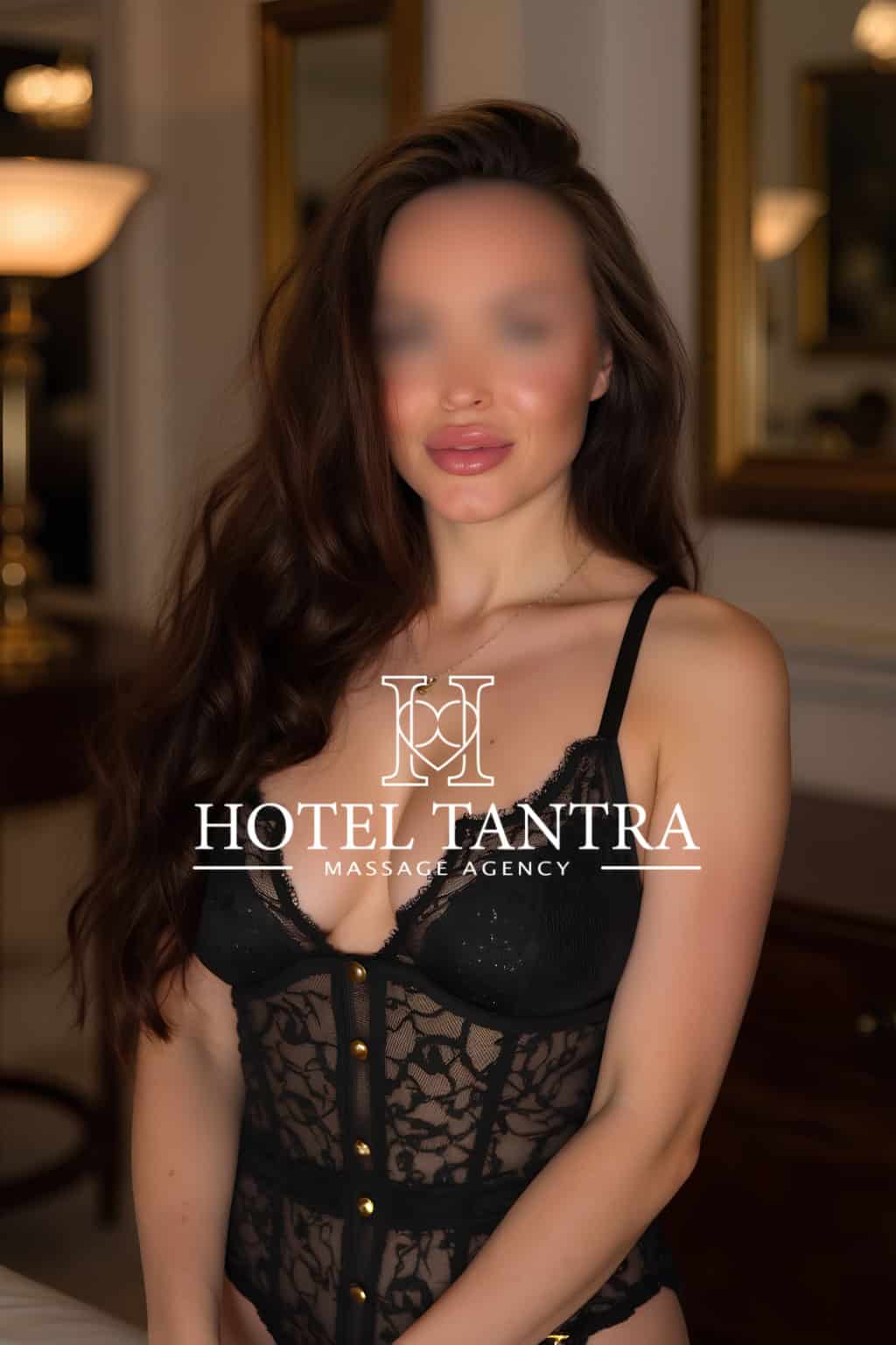 Hotel-tantra-massage-alexandra - Erotic Massage & Outcall Massage in Madrid Woman wearing black lace lingerie stands in a warmly lit room with a watermark reading 'Hotel Tantra Massage Agency'