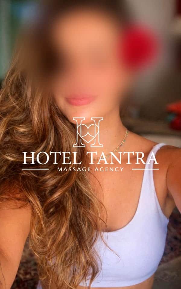 Blurred portrait of a person with long wavy hair wearing a white top, overlaid by the 'Hotel Tantra Massage Agency' logo.