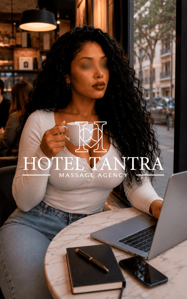 Woman with curly hair sitting at a marble table in a cafe, holding a white coffee cup, with a laptop and notebook nearby; logo and text ' HOTEL TANTRA MASSAGE AGENCY ' displayed across the image (branding scene).