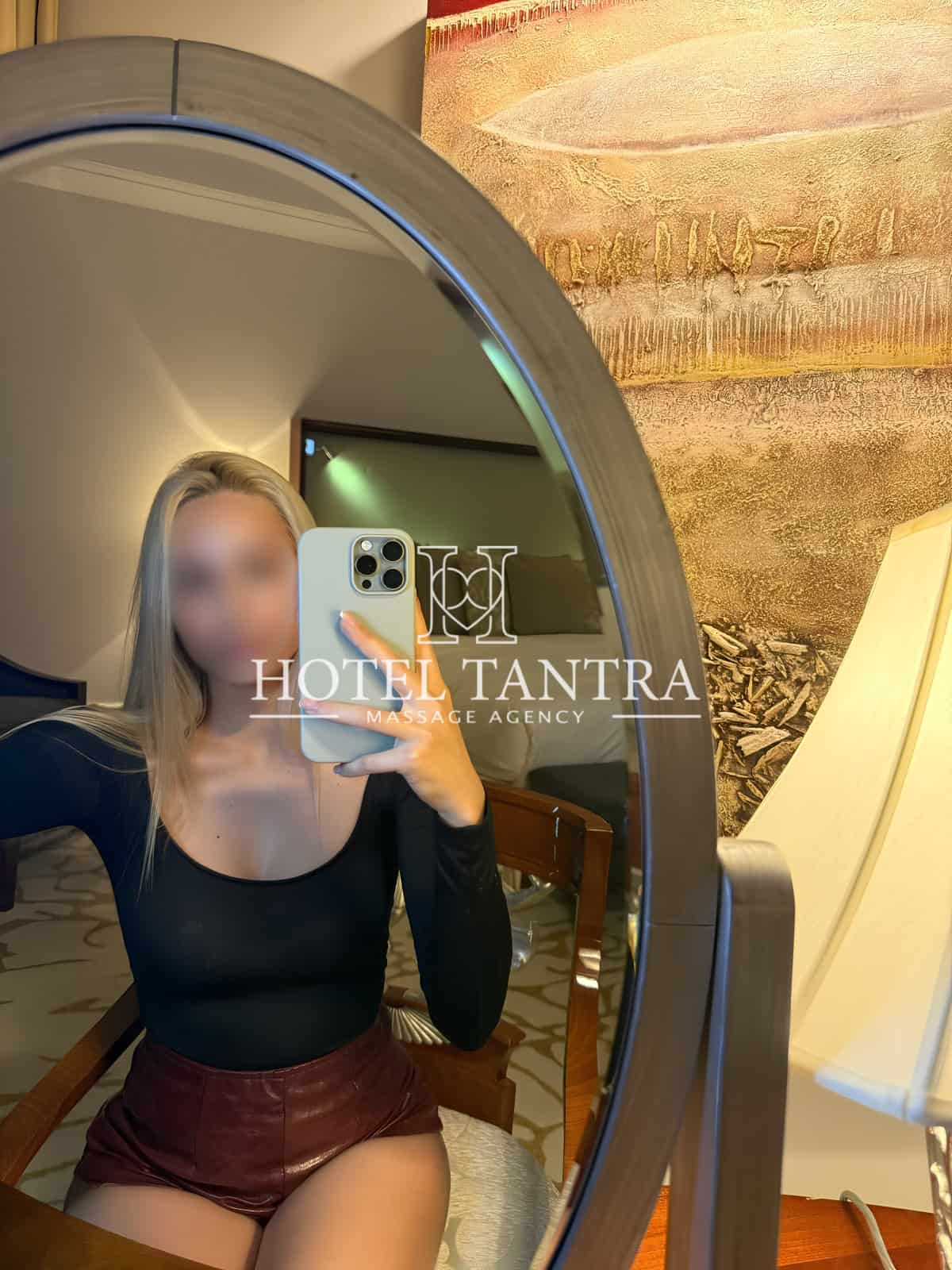 Self-portrait in a circular mirror with a phone, watermark reads 'Hotel Tantra Massage Agency' over the image, blurred face.
